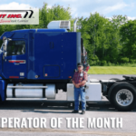 Trailer Transit Inc. | A man stands next to a blue semi-truck adorned with the text "Owner Operator of the Month - August 2021" at the bottom and the "Trailer Transit Inc." logo at the top left. The background features trees and a cloudy sky.