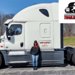 Trailer Transit Inc. | A person stands next to a white tractor-trailer truck. The image includes a banner with text: "OWNER OPERATOR OF THE MONTH" and "TRAILER TRANSIT INC." on the upper right corner, celebrating their achievement.