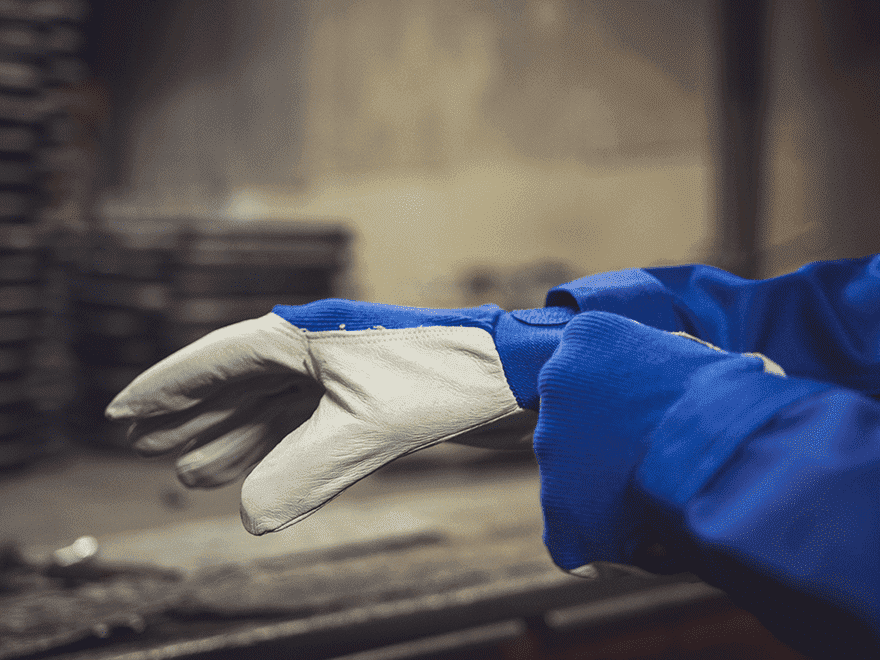 Trailer Transit Inc. | An owner-operator in a blue protective suit adjusts a white work glove in an industrial setting.