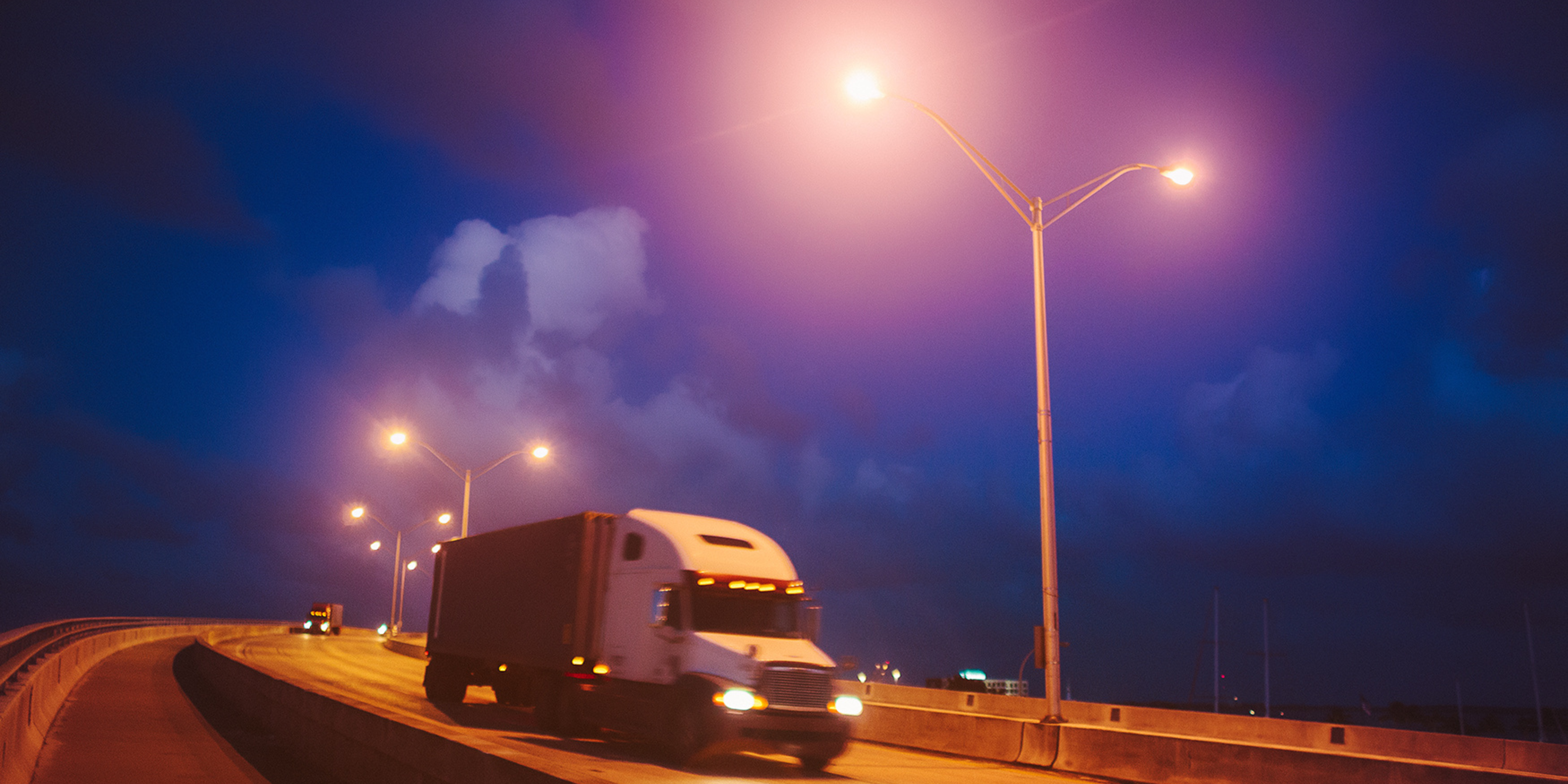 Trailer Transit, Inc | semi trucks driving in the late evening with street lights on