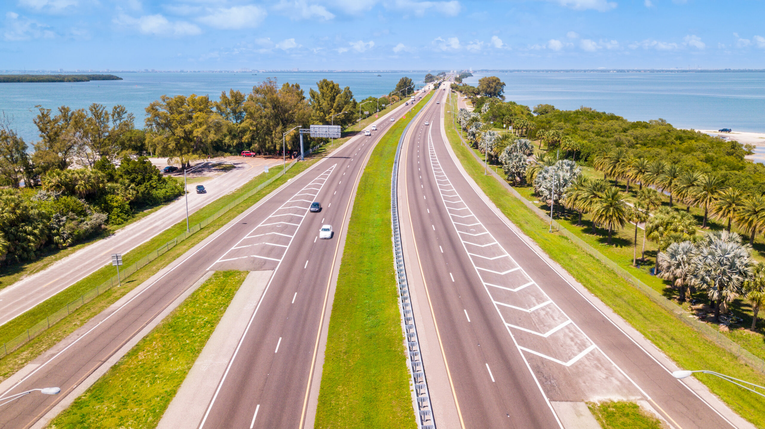 Trailer Transit Inc. | Aerial view of a wide, divided highway with few vehicles, surrounded by greenery and water on a clear day.