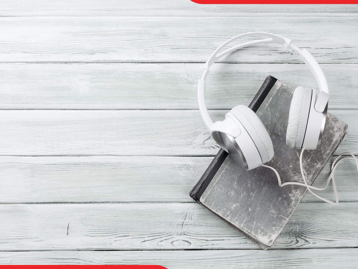 Trailer Transit Inc. | White headphones resting on a closed hardcover book on a light wooden surface with two red corners framing the image.