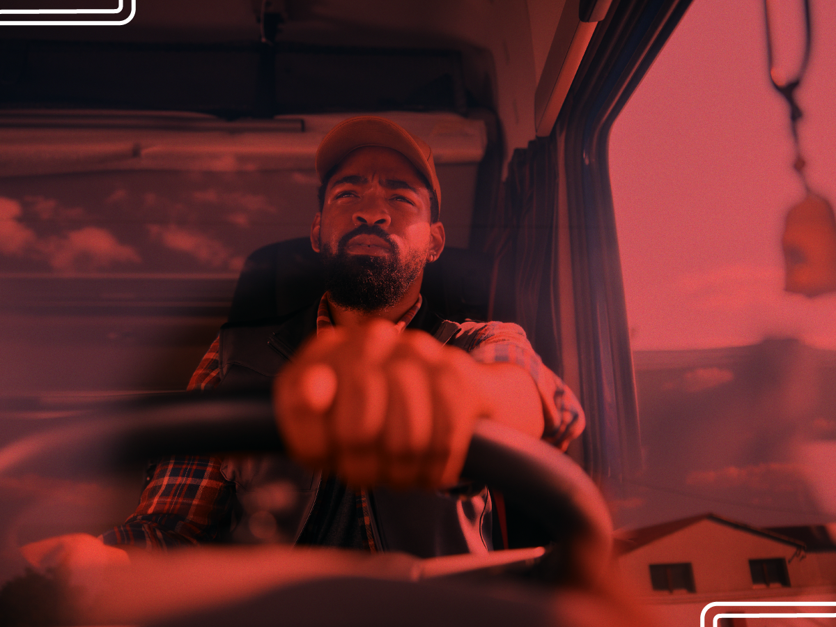 Trailer Transit Inc. | A man is driving a vehicle, gripping the steering wheel. The image has a red tint, and there is a window reflection showing buildings outside.