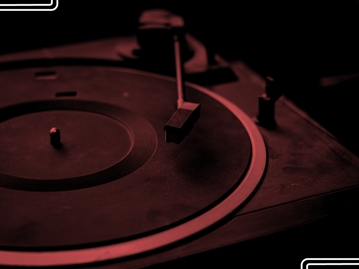 Trailer Transit Inc. | Close-up of a vintage turntable with a dark red filter. The tonearm is positioned over the empty platter.