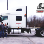 Trailer Transit Inc. | Driver Howard and his wife stand beside their large white semi-truck, with the "Trailer Transit Inc. Owner Operator of the Month" logo displayed in the top right corner.